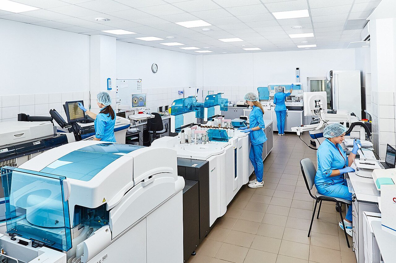 Quality assurance laboratory technician conducting microbial screening under a microscope