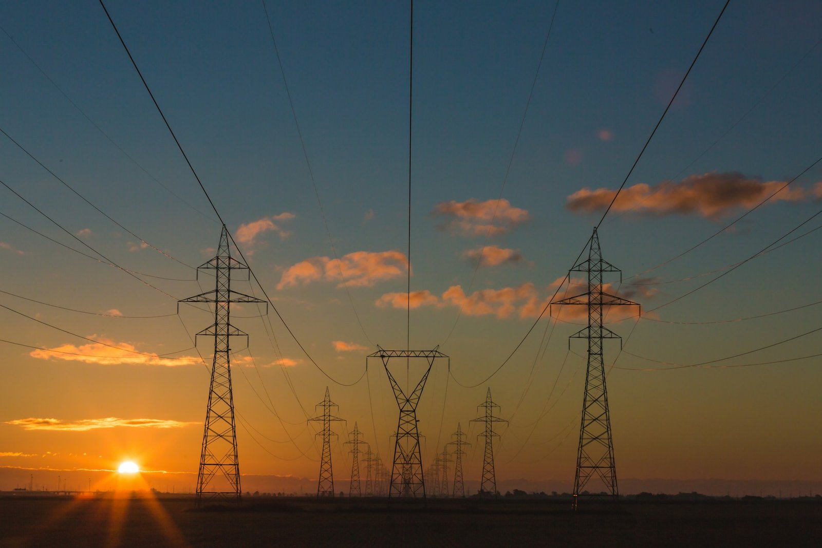 High-voltage electrical transmission towers and steel lattice infrastructure spanning a rural utility corridor